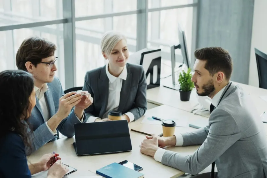 A manager leads a team meeting in a bright modern office, with colleagues collaborating around a table.